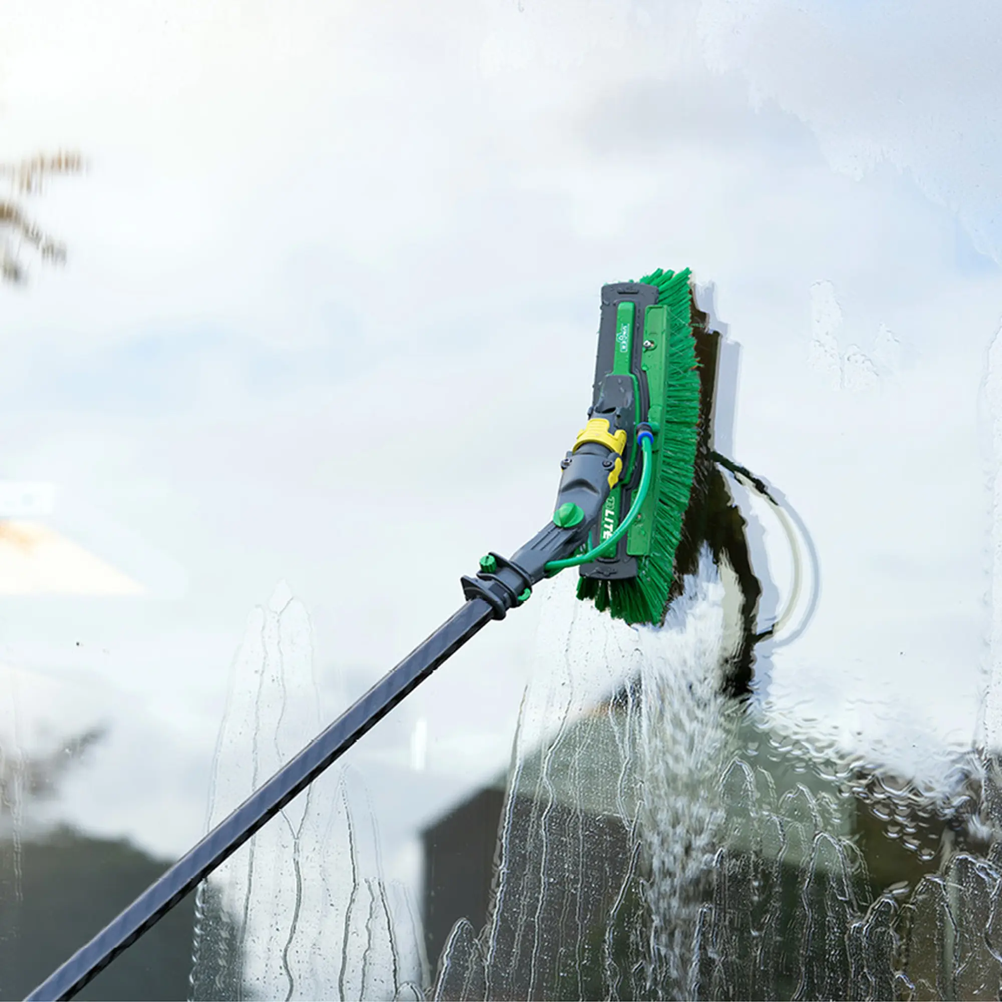 Unger nLITE Power Bürste komplett grün beim Reinigen einer Glasfläche mit Wasser, innovative Power-Bürste von Unger für gründliche Fensterreinigung
