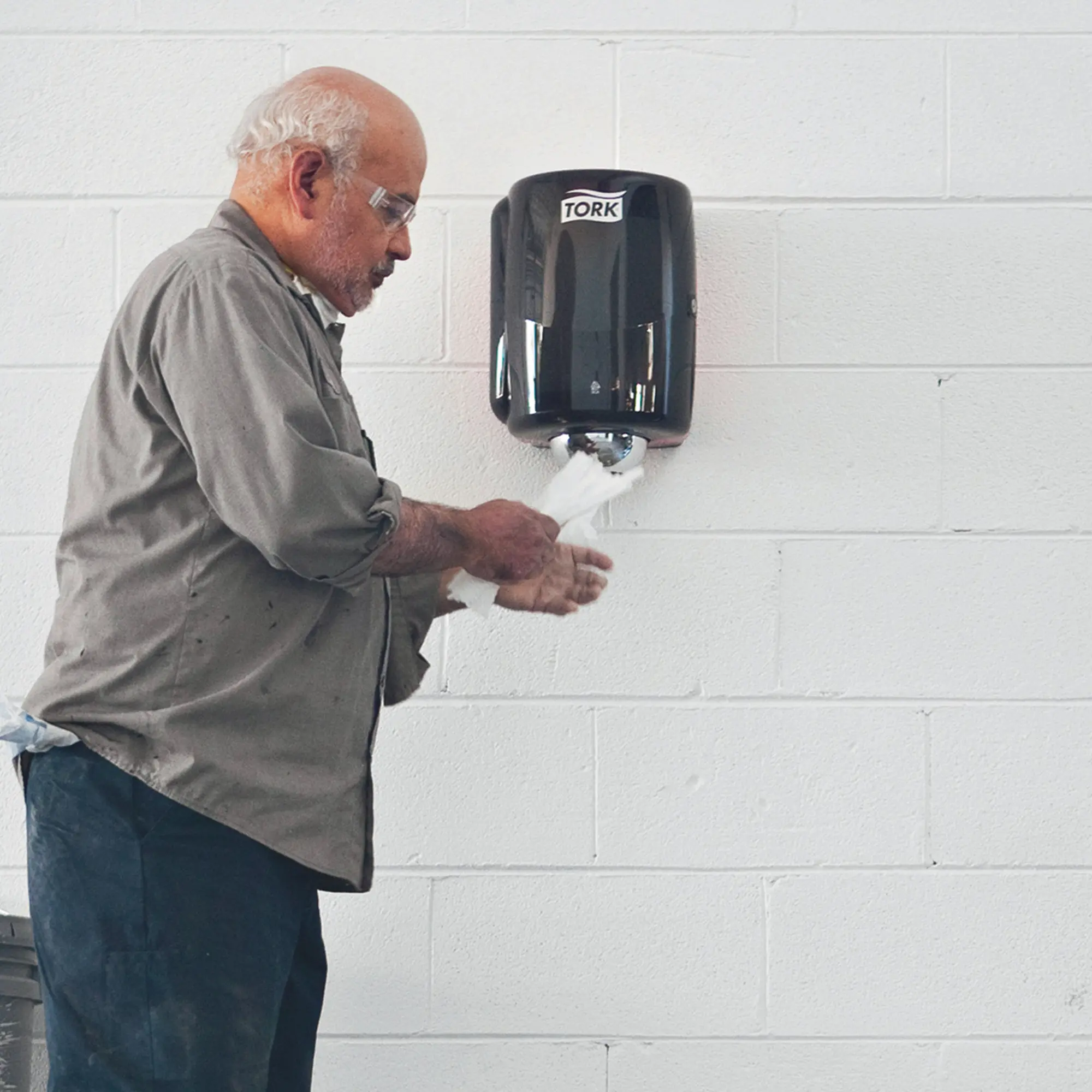 Tork Performance Maxi-Innenabrollungsspender W2 an der Wand, ein Anwender entnimmt einhändig Papier aus der W2-Centerfeed-Rolle, Artikelnr. 653000/653008