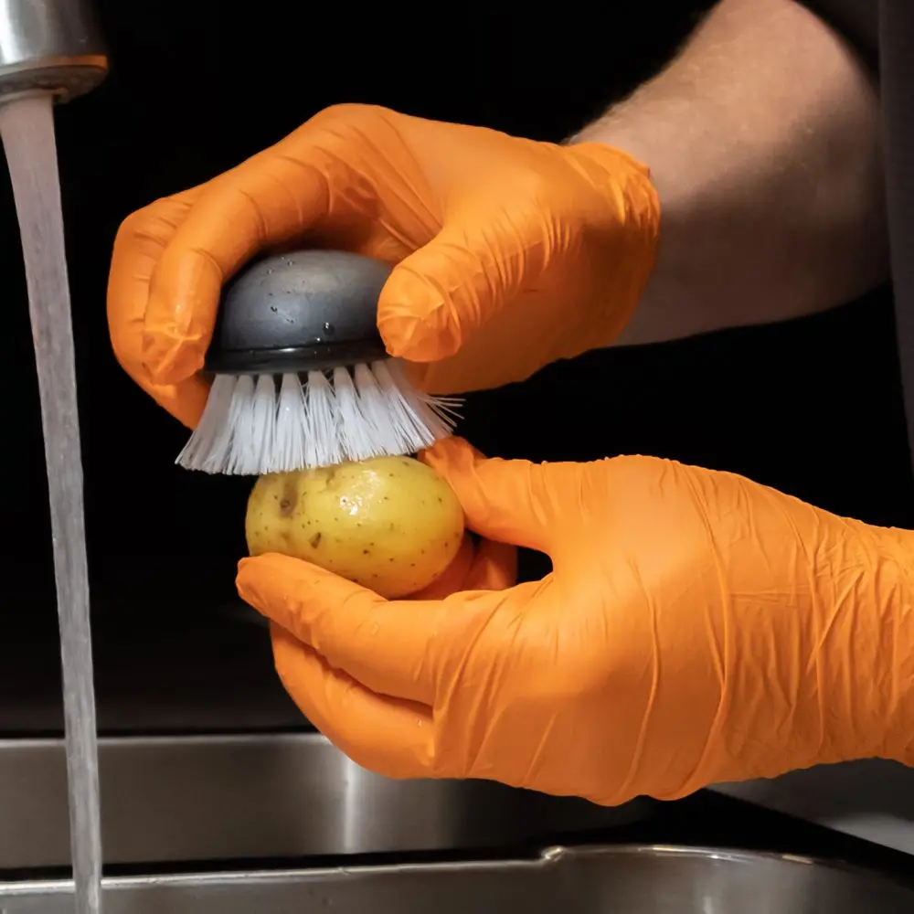 Hygostar Safe Light Nitrilhandschuhe orange puderfrei beim hygienischen Reinigen einer Kartoffel unter fließendem Wasser in der Küche, VE 1000 Stück