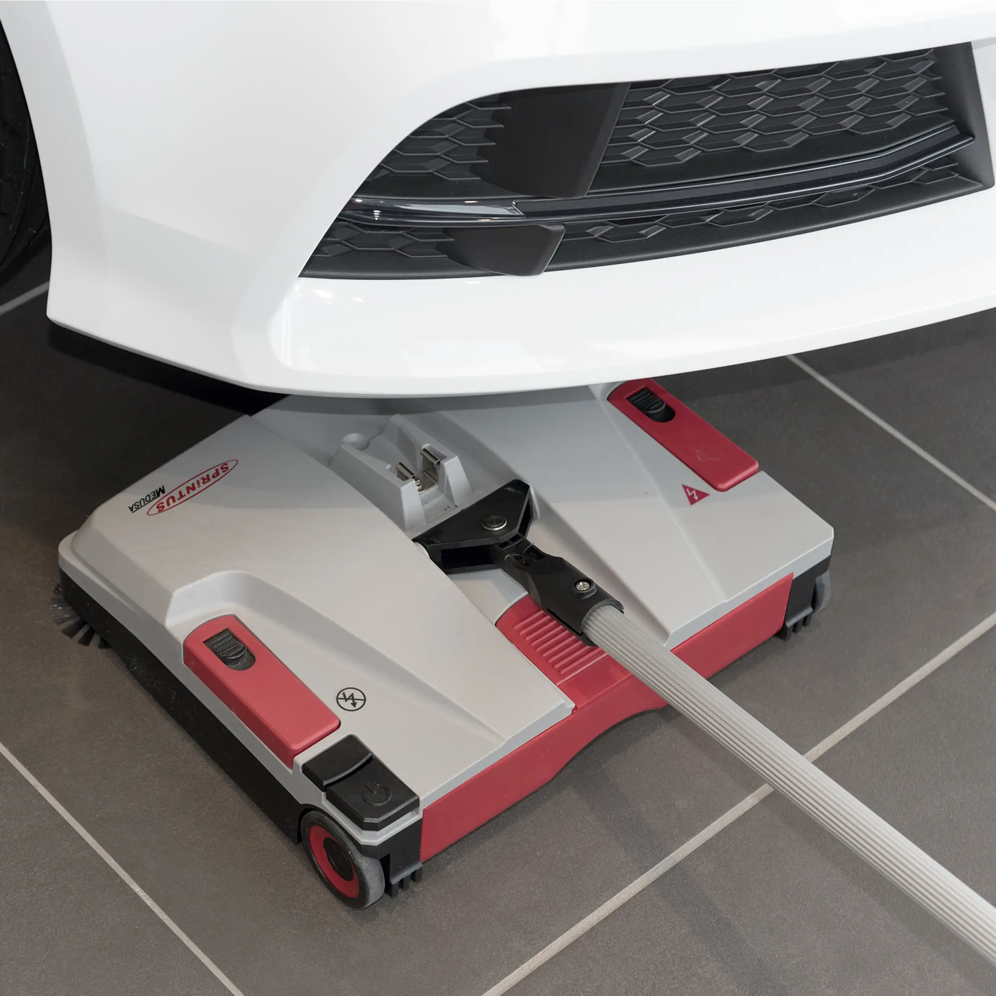 Sprintus Akkukehrmaschine Medusa beim kabellosen Kehren von Hartboden unter einem Fahrzeug, professionelle akkubetriebene Kehrmaschine für Innen- und Außenbereiche