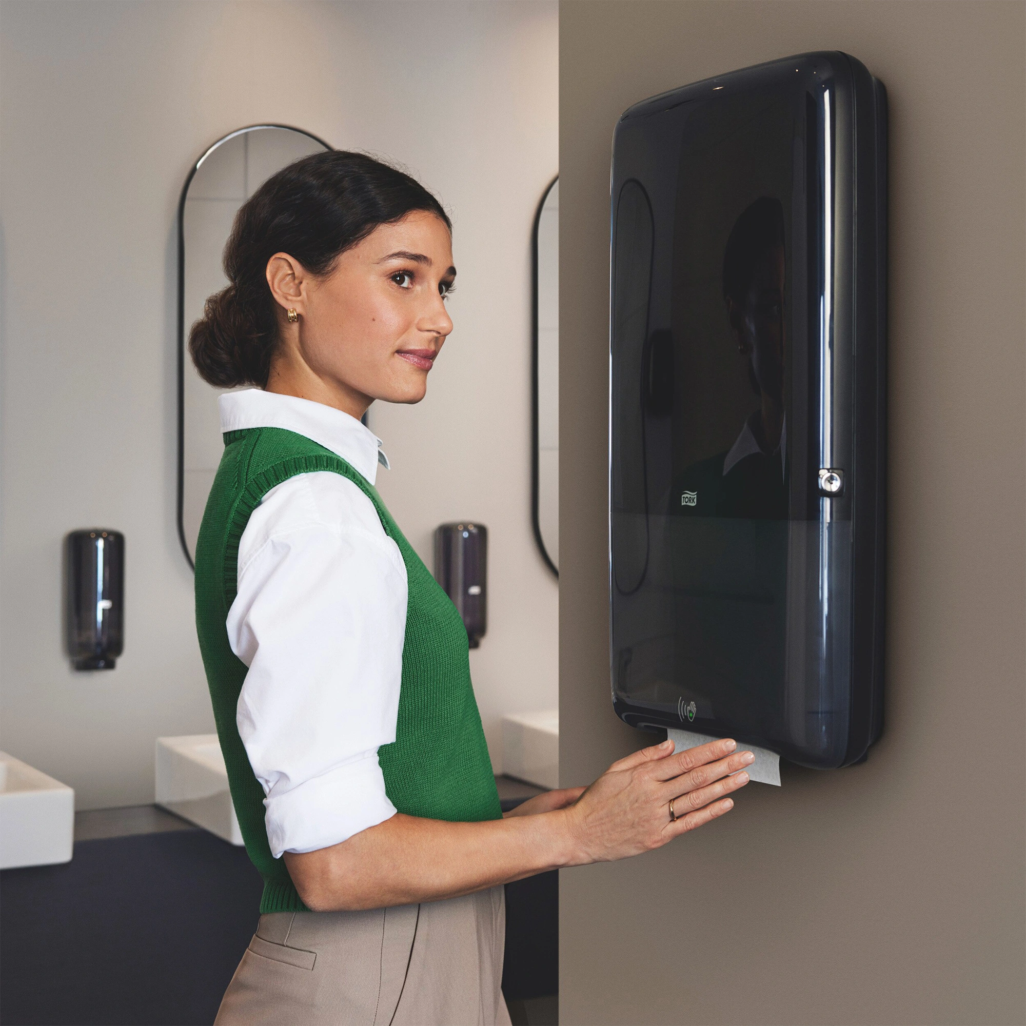 Tork PeakServe Automatik Handtuchspender H5 von Tork an der Wand in einem modernen, hochfrequentierten Waschraum, Frau entnimmt berührungslos ein Papierhandtuch, geeignet für 1.230 Tücher, Art.-Nr. 552504