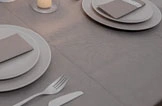 Graue Tischdecke auf elegant gedecktem Tisch mit Tellern, Servietten, Besteck und Kerze, ideal für festliche Anlässe
