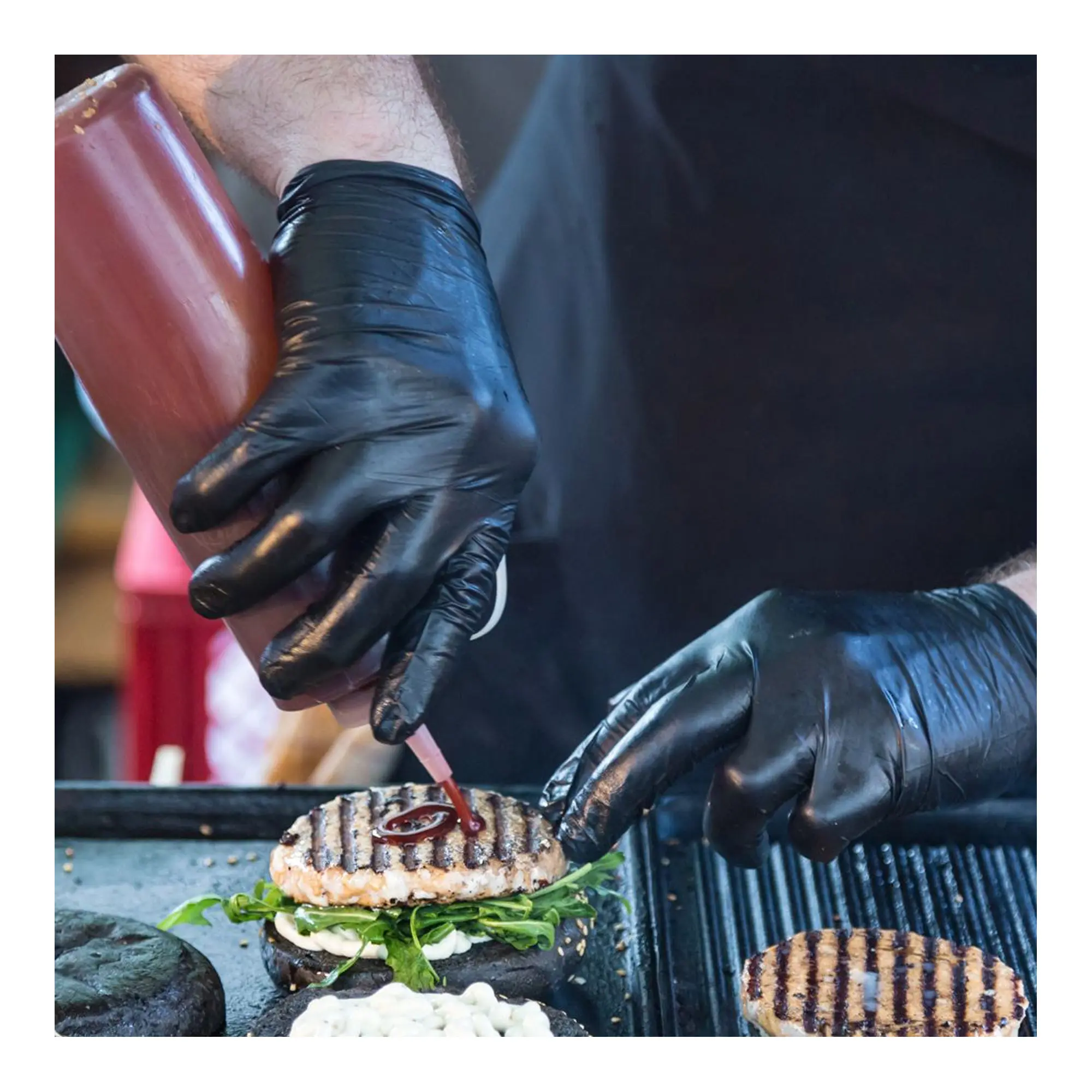 Hygostar Diablo Latexhandschuhe schwarz puderfrei, VE 1000 Stück – Koch mit schwarzen Latex-Einweghandschuhen beim hygienischen Belegen und Garnieren eines Burgers am Grill