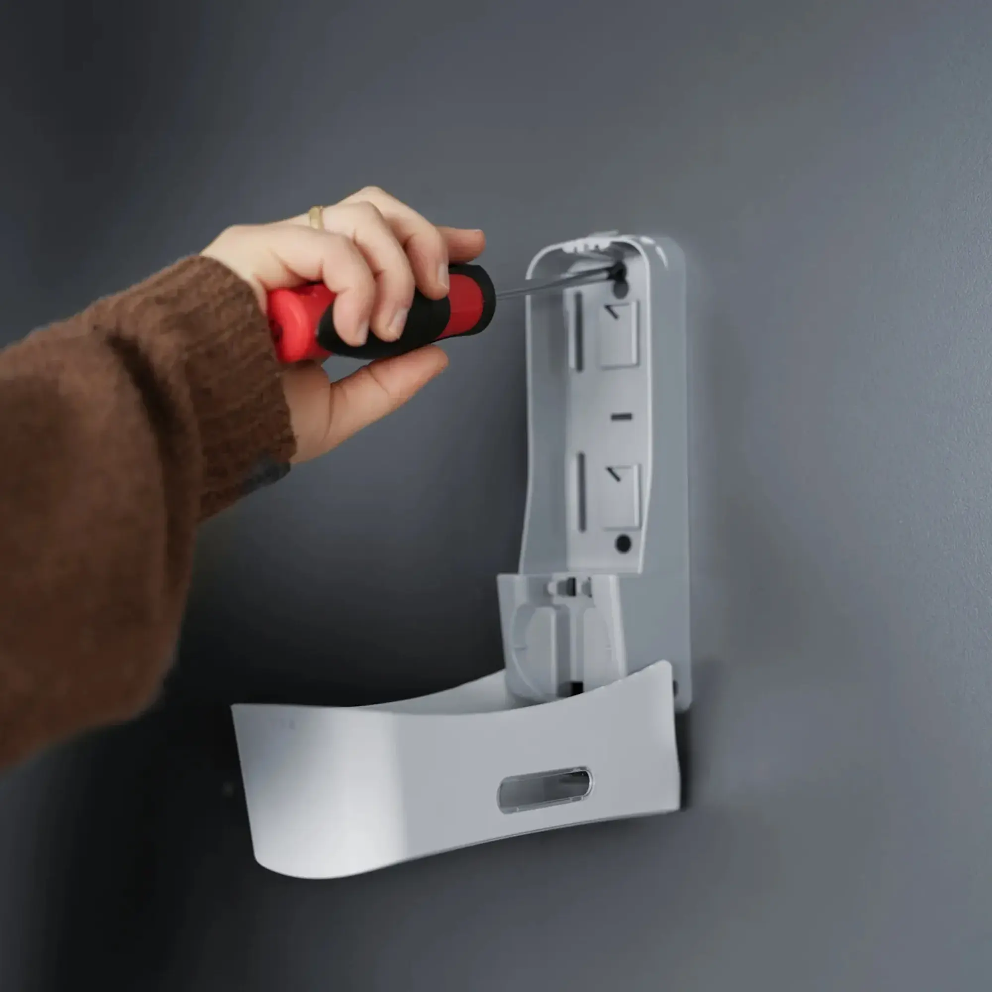 SEMYtop Dusch- u. Badspender 350 ml Kunststoff, Wandmontage eines weißen Spenders aus der Black & White Hygienespender-Linie mit Schraubendreher an einer grauen Wand